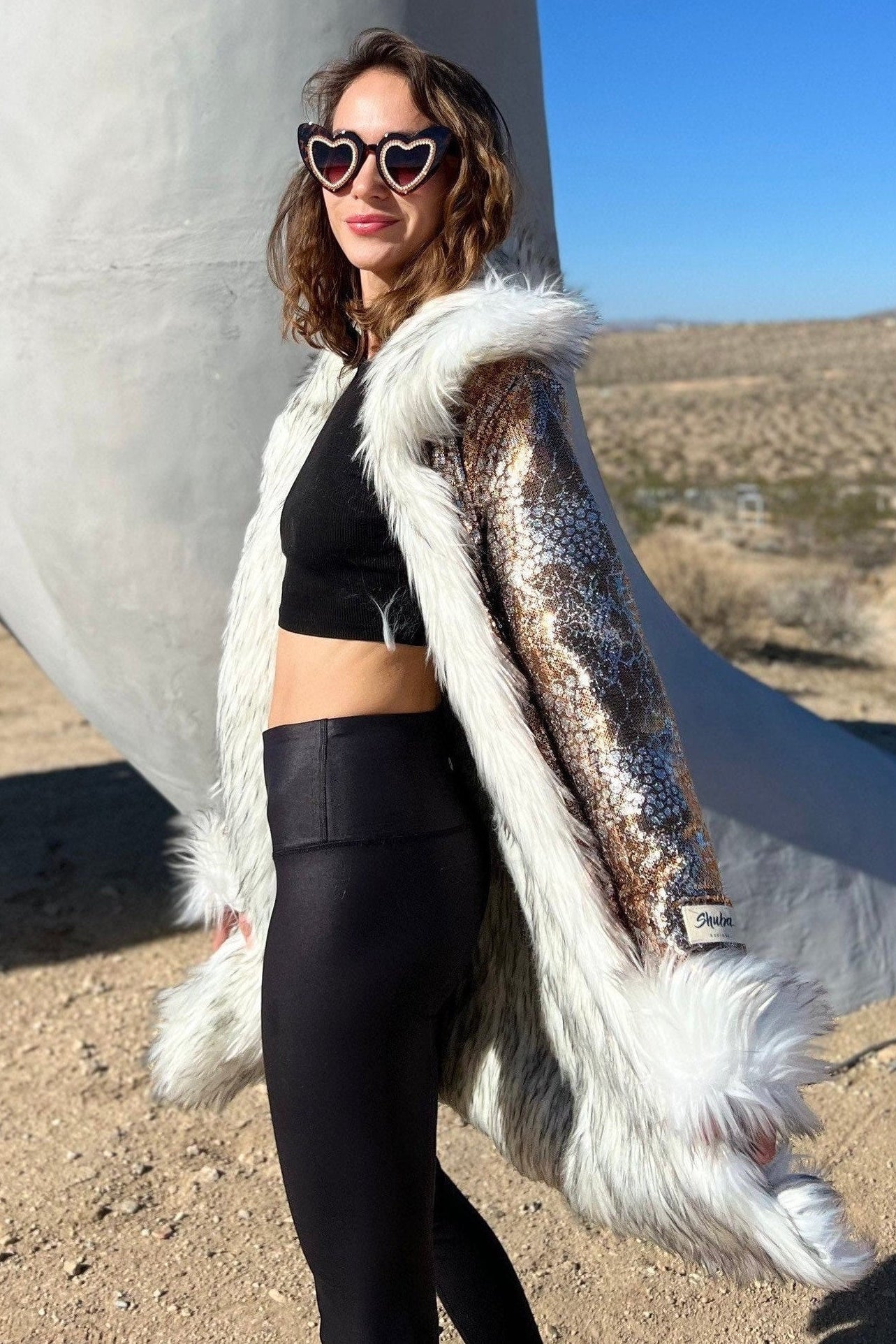 Woman in a stylish outfit with a fur coat and black leggings standing in a desert landscape.