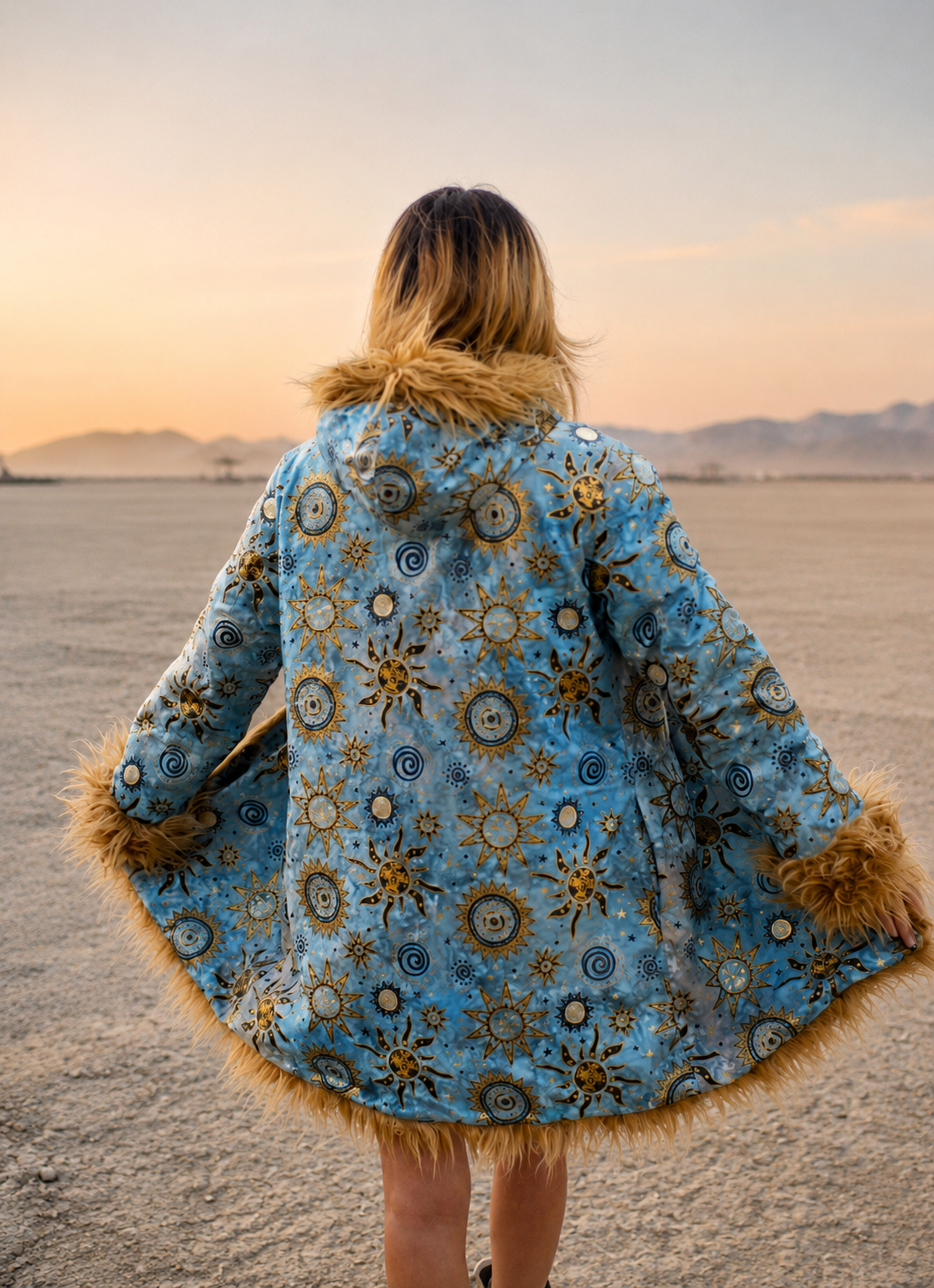 Blue patterned Burning Man coat for women, reversible faux fur playa jacket with tan fur trim, back view in the desert