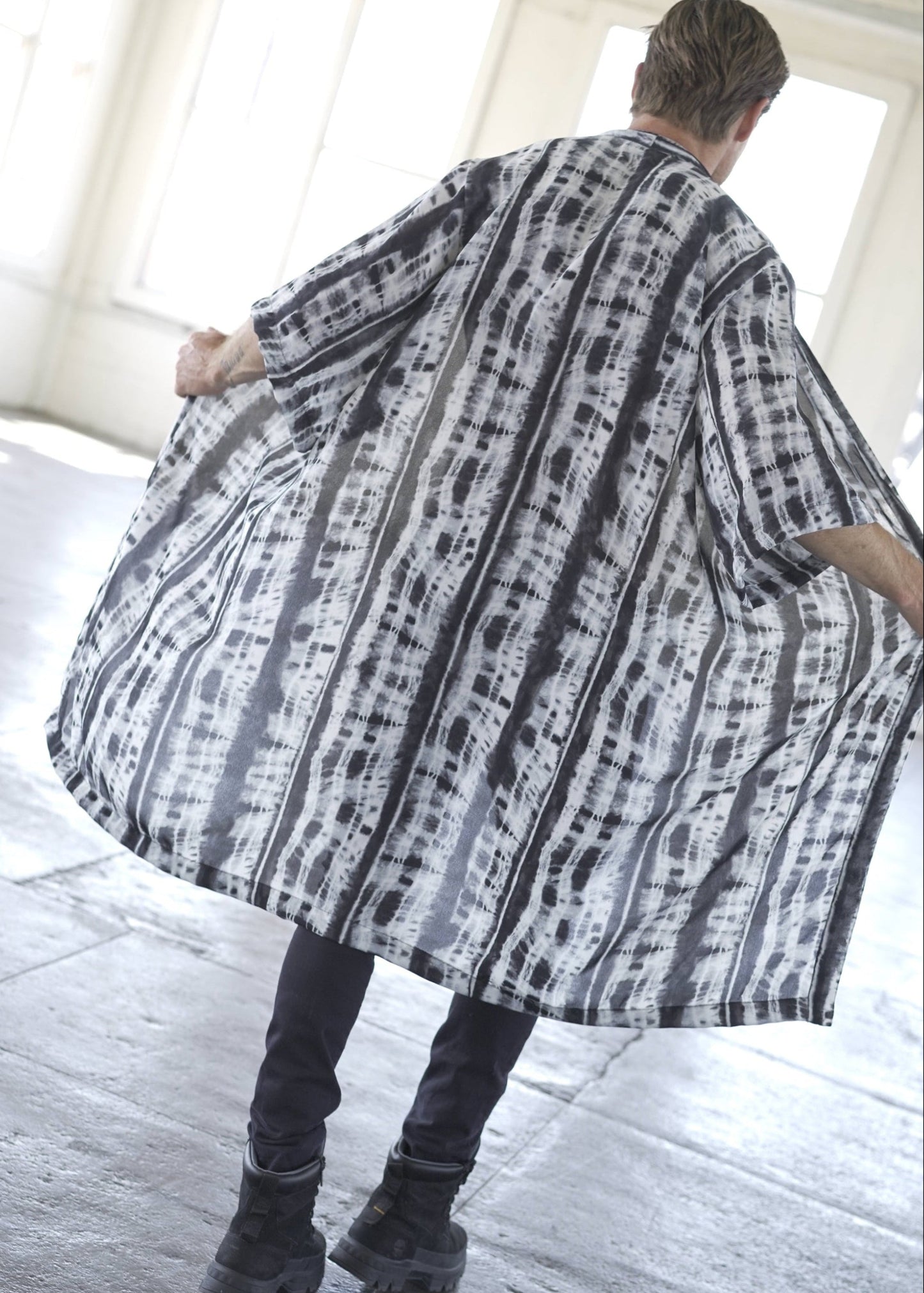 Man wearing a long, patterned coat in a bright room.
