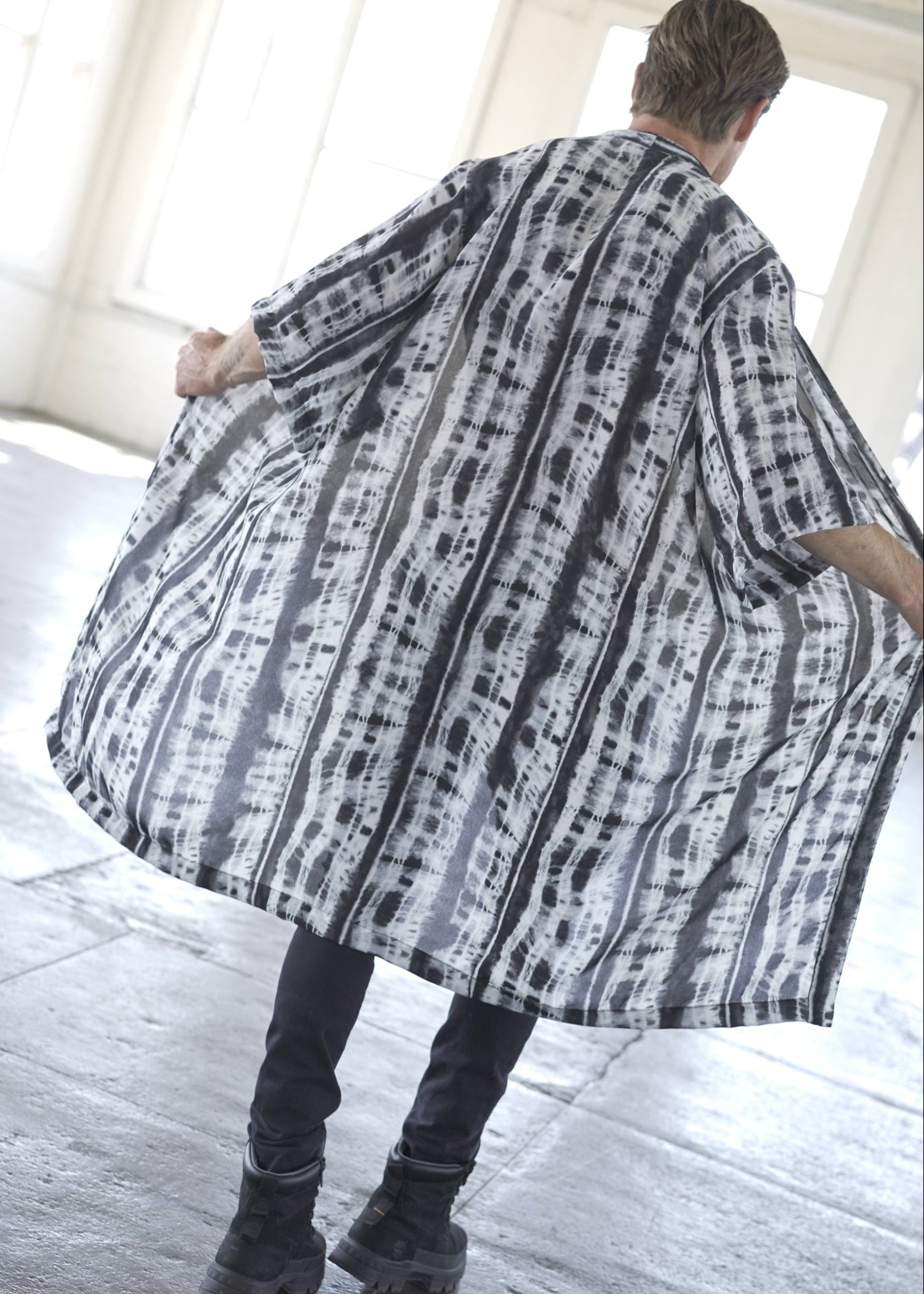 Man wearing a long, patterned coat in a bright room.